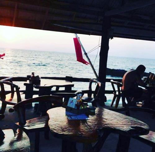 a man sitting at a table in front of the ocean at Lanta New Beach Bungalows - SHA Plus in Ko Lanta