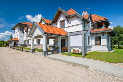 a white house with orange roofs on a gravel road at Hotel Joseph Conrad SPA & Wellness in Pisz