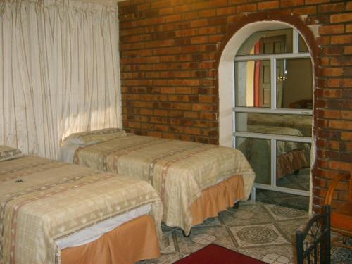 Habitación con 2 camas y pared de ladrillo en All Are Welcome Guest House en Brakpan