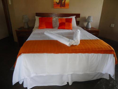 a large bed with orange and white sheets and pillows at Noma-Nini Lodge in White River