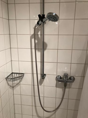 a shower with a hose in a white tiled bathroom at Apartments Altstadtflair in Regensburg