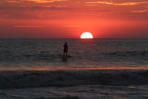 a man standing on a paddle board in the ocean at sunset at Palm Coast Luxury Rentals in Esterillos Este