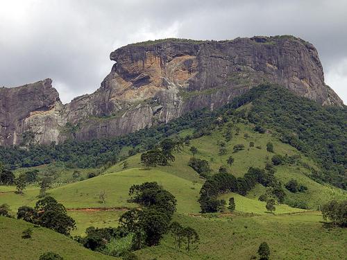 a green hill with a mountain in the background at Pousada Rota dos Pássaros in São Bento do Sapucaí