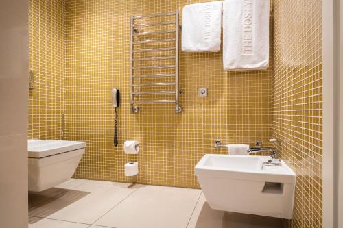 a bathroom with a sink and a toilet and yellow tiles at The Dostyk Hotel in Almaty