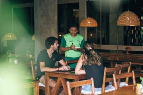 two men and a woman sitting at a table in a restaurant at Grandmas Plus Hotel Airport in Kuta