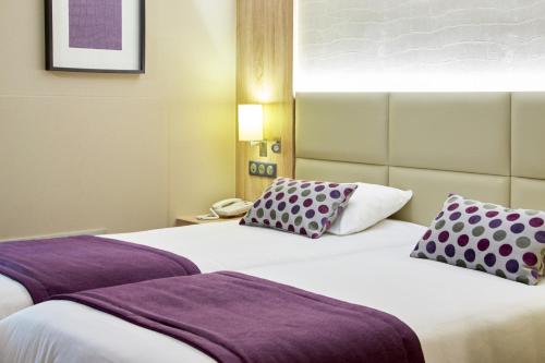 2 bedden in een hotelkamer met paarse kussens bij Kyriad Beaune in Beaune