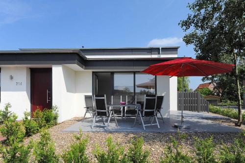 ein Haus mit einem Tisch, Stühlen und einem roten Regenschirm in der Unterkunft Haus Kunterbunt in Bensersiel