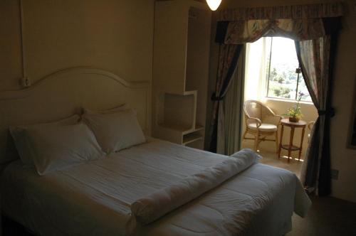 um quarto com uma cama branca e uma grande janela em Pousada do Verde Gramado em Gramado