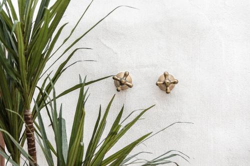 two gold hooks on a white wall with a plant at S'Hotelet d'es Born - Suites & SPA in Ciutadella