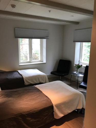 a bedroom with two beds and a chair and two windows at Mullbärsgårdens Bed and Breakfast in Visby