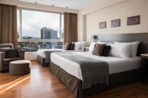 two beds in a hotel room with a large window at Dazzler by Wyndham Puerto Madryn in Puerto Madryn