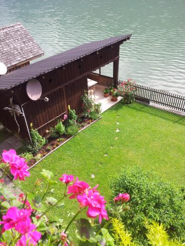 a wooden pavilion next to the water with pink flowers at Fewo Wakolbinger-Wieder in Hallstatt