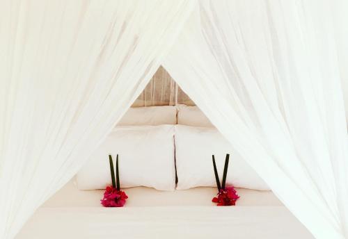 uma cama branca com cortinas brancas e flores cor-de-rosa em Manusia Dunia Green Lodge em Gili Air