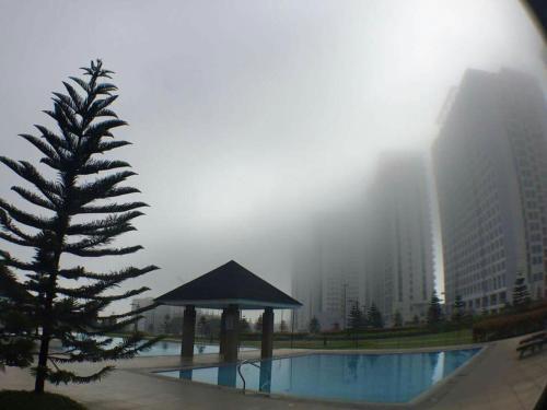 a foggy view of a pool with a tree and a building at AMS Staycation at Wind Residences in Tagaytay