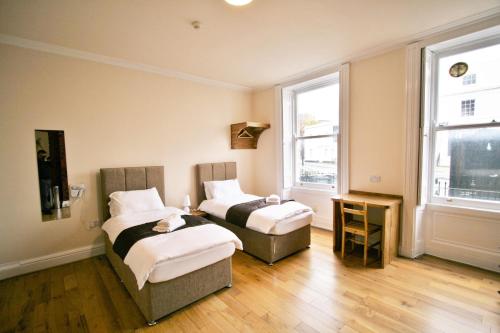 two beds in a room with two windows at Central Studios Gloucester Place by Roomsbooked in Cheltenham