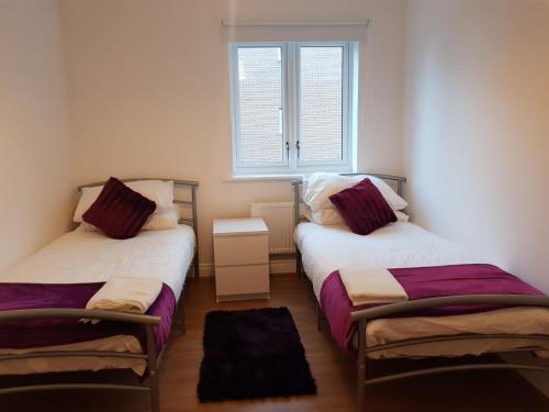 two beds in a small room with a window at Vetrelax Chelmsford Apartment in Chelmsford
