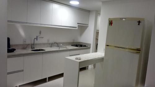 uma cozinha com armários brancos e uma geladeira em Apartamento frente para a piscina a uma quadra da praia em Florianópolis