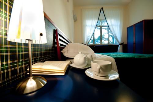 a table with a lamp and two cups and a book at Hotel Villa Sturzo in Caltagirone