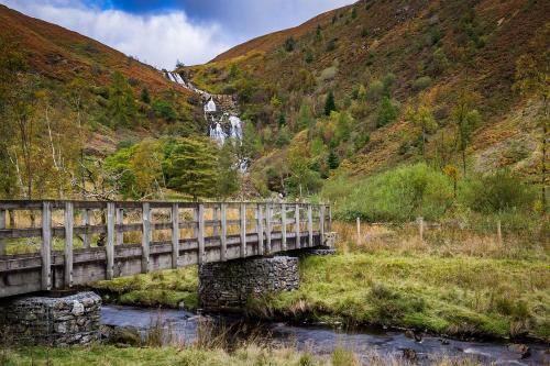 a bridge over a river with a waterfall in the background at Lake Vyrnwy Hotel & Spa in Llanwddyn
