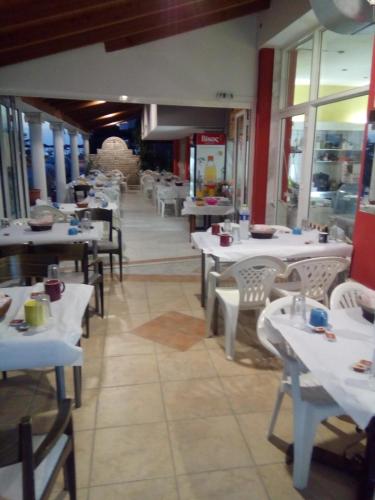 ein Restaurant mit weißen Tischen und Stühlen und Fenstern in der Unterkunft Hotel Ifigenia Paralia Katerinis plaz in Paralia Katerinis