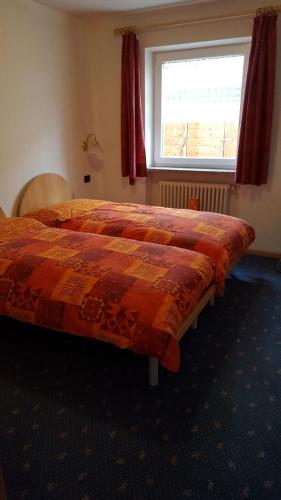 a bed with an orange comforter in a room with a window at Cèsa Chri e Sofì in Campitello di Fassa