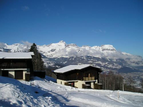 un edificio cubierto de nieve con montañas en el fondo en La Grange N° 27 - Bât. 6, en Combloux