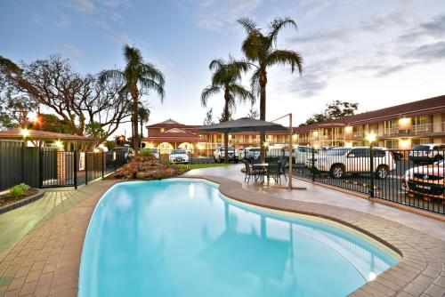 a pool in front of a hotel with palm trees at The Aberdeen Motel in Dubbo