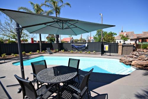 a table and chairs with an umbrella next to a pool at The Aberdeen Motel in Dubbo