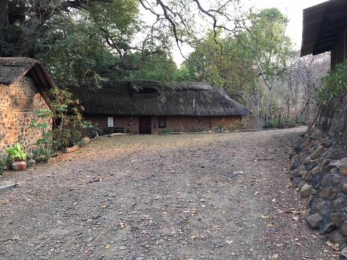 a house with a thatched roof and a dirt road at Sundowner Lodge in Hwange