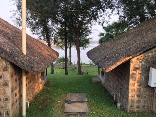 two stone buildings with trees in a field at Sundowner Lodge in Hwange