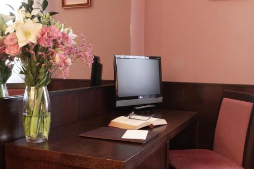 a desk with a vase of flowers and a computer monitor at Hotel City in Piacenza