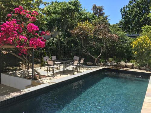 a pool with chairs and a table and pink flowers at Villa Honeysuckle Luxury 4 Bedroom in Stellenbosch