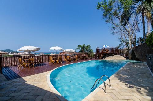 a swimming pool with tables and umbrellas and the ocean at Hotel Coquille in Ubatuba