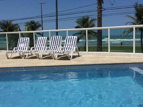 three white chairs sitting next to a swimming pool at Residencial Viamar in Praia Grande