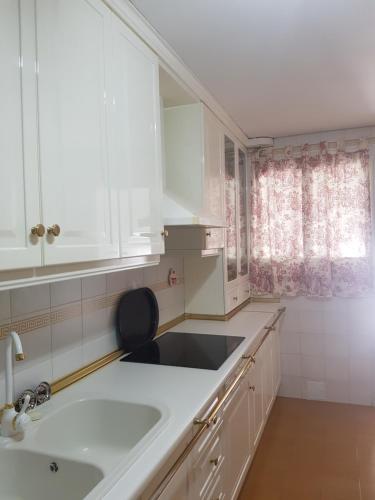 uma cozinha com armários brancos, um lavatório e uma janela em Apartamento Eduardo Dato em Sevilha