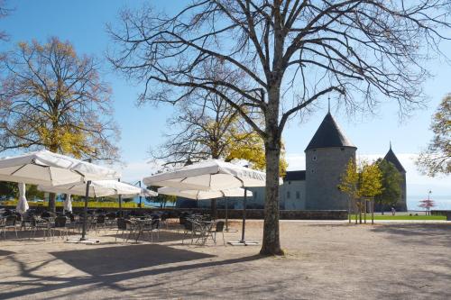 a table and chairs with umbrellas and a castle at L'Hôtel by Hostellerie du Château in Rolle