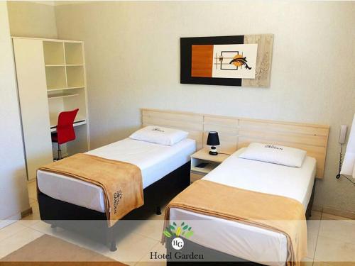 Una habitación de hotel con dos camas y una silla roja. en Hotel Garden, en Santa Maria