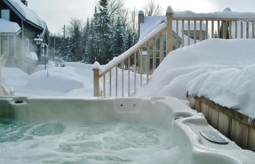 a hot tub covered in snow next to a house at Chalet 9006 Chemin des Alpages by Les Chalets Alpins in Stoneham
