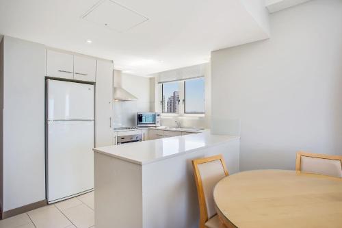 a white kitchen with a table and a white refrigerator at Mantra Twin Towns in Tweed Heads