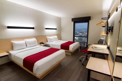 a hotel room with two beds and a desk and a window at City Express Plus by Marriott Ciudad de México Mundo E in Mexico City