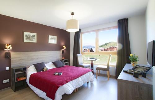 a bedroom with a red bed and a desk and a window at Résidence Prestige Odalys Front de Neige in Plagne Villages
