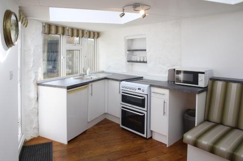 a kitchen with white cabinets and a sink and a microwave at Little Trewin in Helston