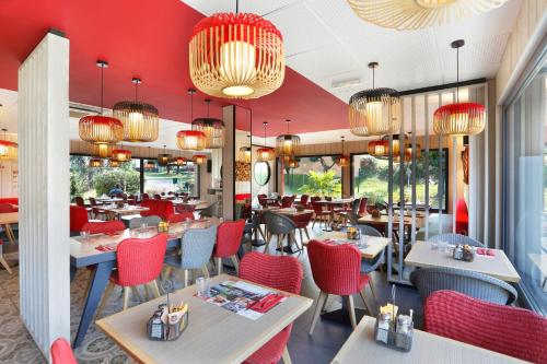 ルマンにあるイビス ル マン エスト ポントリューの赤い椅子とテーブル、シャンデリアのあるレストラン