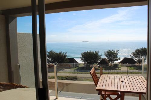 een balkon met een tafel en uitzicht op de oceaan bij Seafront Apartment in Mossel Bay in Mosselbaai