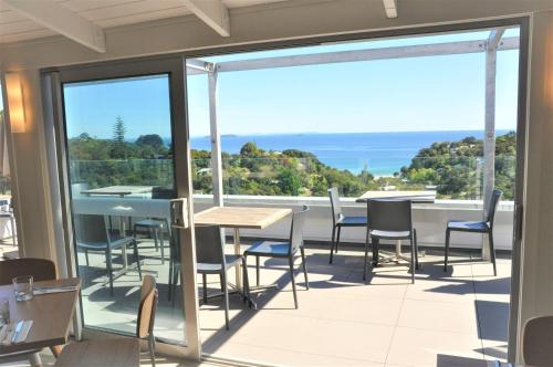 a balcony with tables and chairs and a view of the ocean at Villa Rosa at Palm Beach by Waiheke Unlimited in Palm Beach