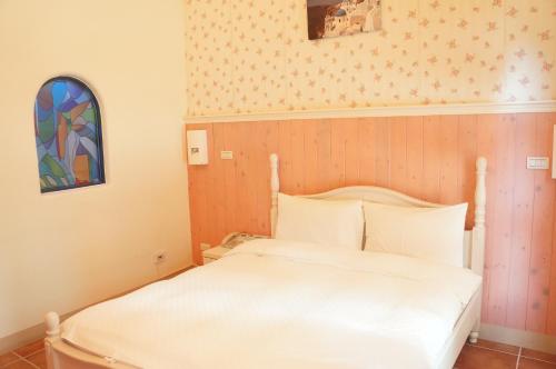 a small bedroom with a white bed and a stained glass window at Rainbow B&B in Dahan