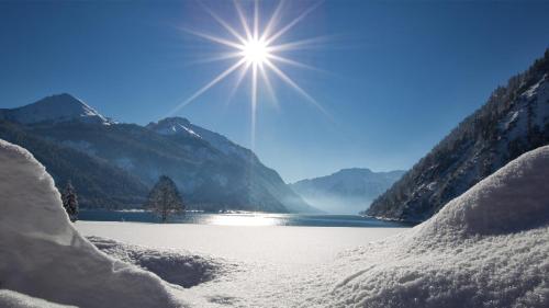 a sun shining over a snow covered lake with mountains at Landhaus Appartement Kofler Ferienwohnungen,Zimmer in Maurach