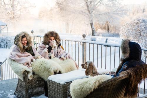 three people sitting on a fence with sheep in the snow at Klækken Hotel in Hønefoss