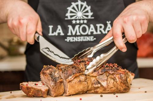 a man cutting a steak with a knife and fork at Pensiunea La Moară in Fundu Moldovei