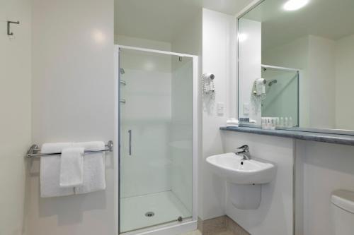 a white bathroom with a shower and a sink at Quest Dunedin Serviced Apartments in Dunedin